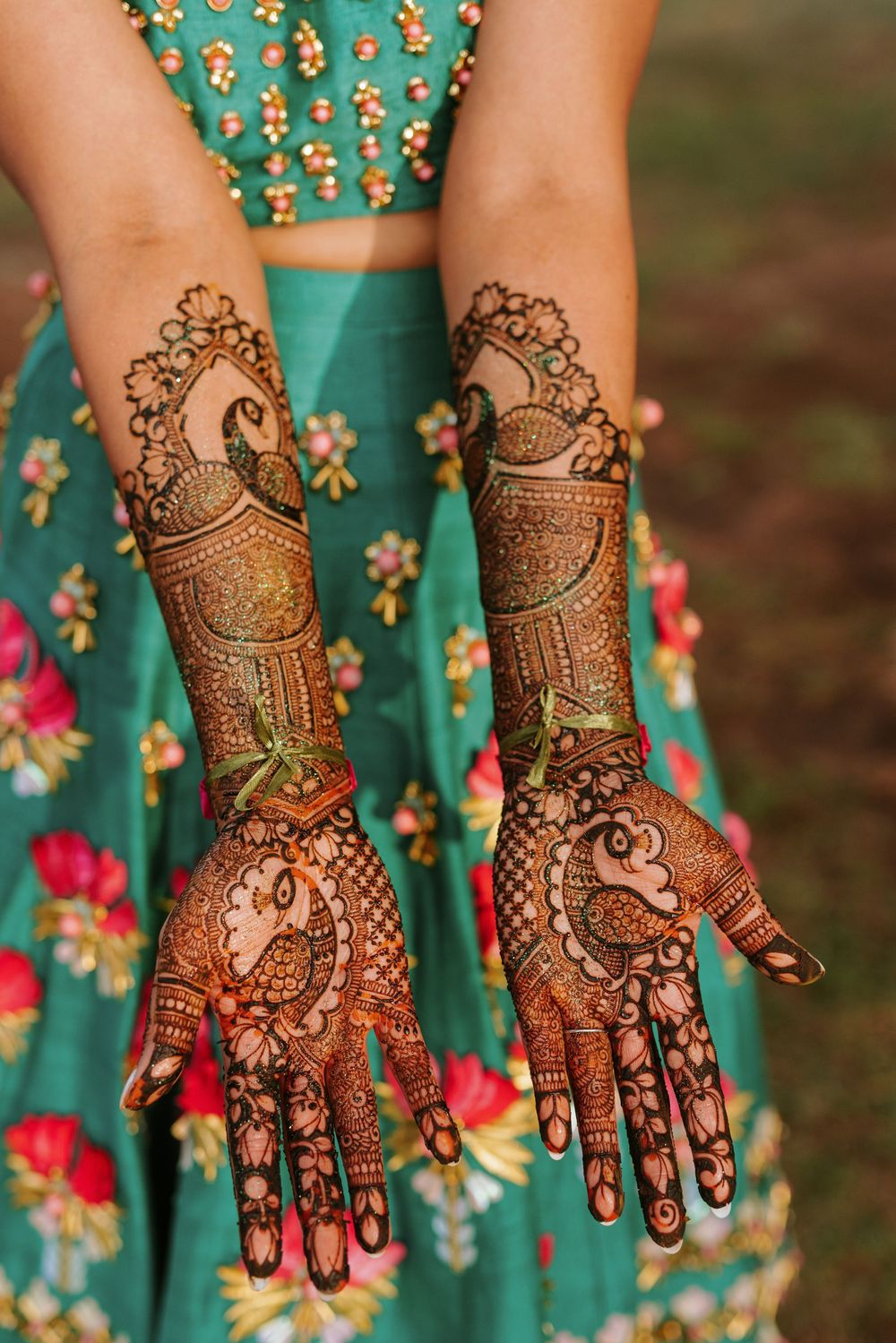 Intricate bridal mehndi henna designs displayed on hands against a turquoise and floral fabric background.