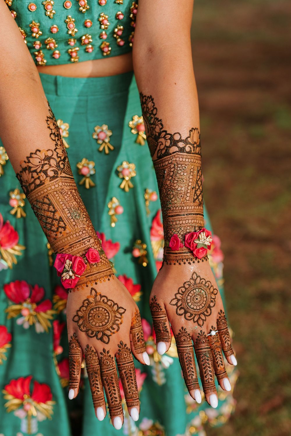 Intricate henna mehndi designs adorned on hands wearing turquoise and pink floral dress.