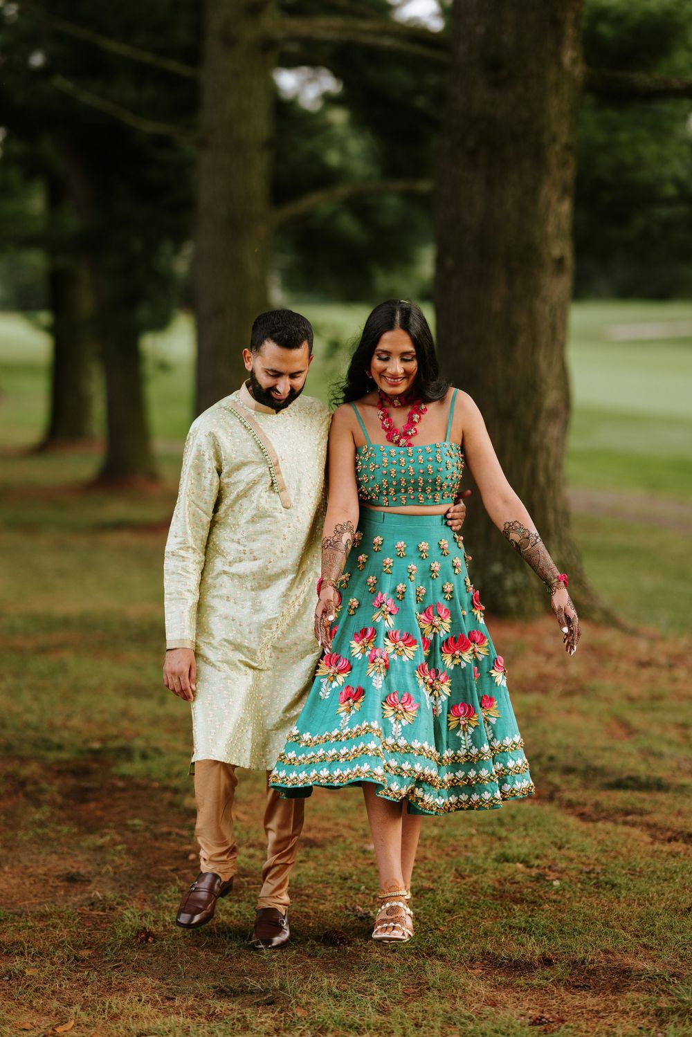 Couple walking together in outdoor setting wearing coordinated turquoise and cream traditional outfits.