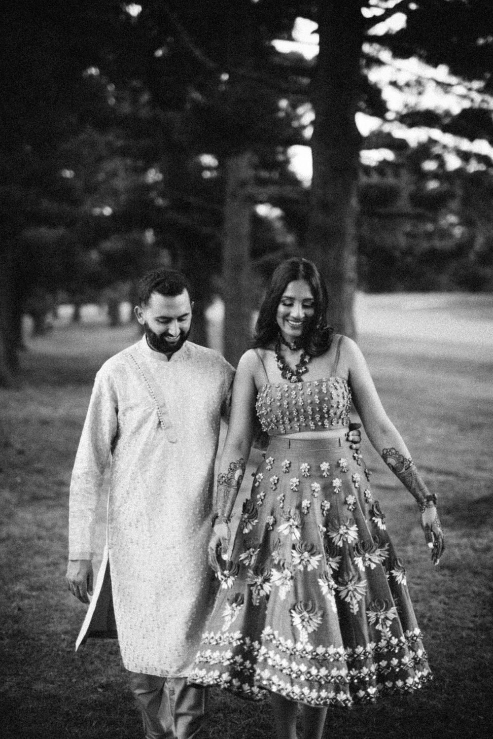 Black and white engagement photos of a couple walking together in a park, with the woman wearing a floral dress.