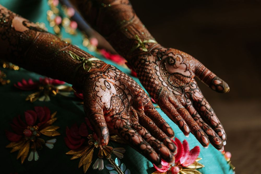 Hands adorned with intricate henna designs rest on a vibrant floral patterned fabric.