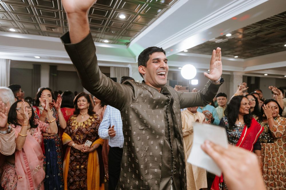 A group of people dancing and celebrating together in an indoor venue with exposed ceiling and bright lighting.