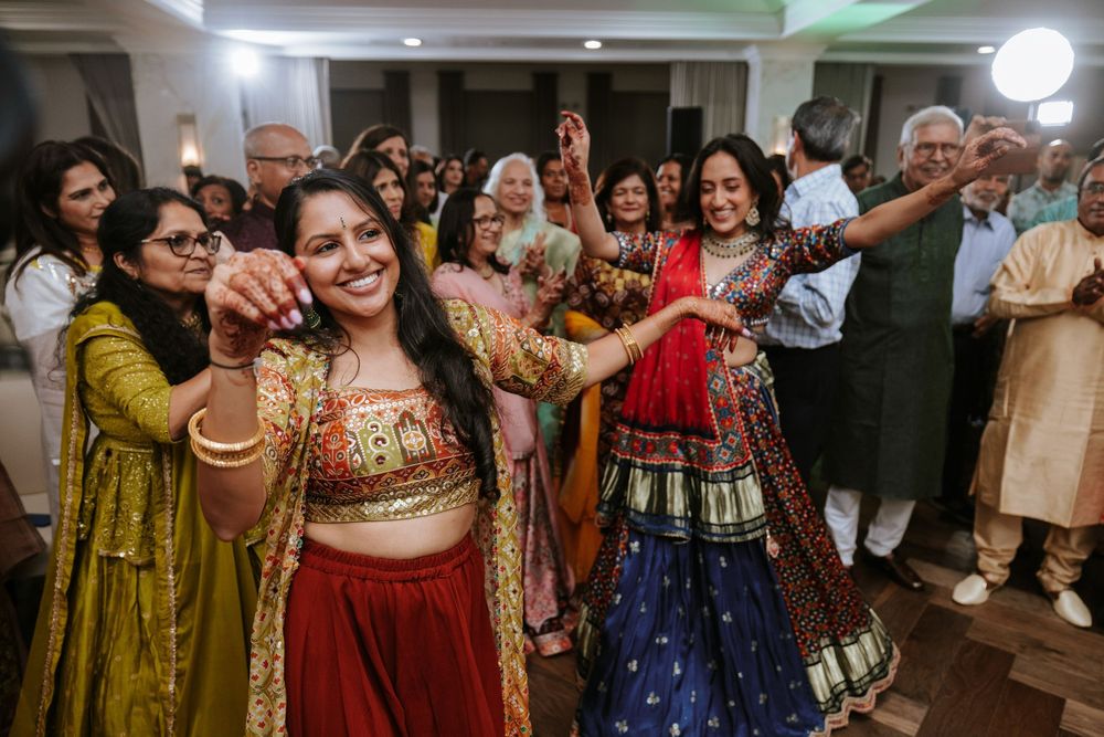 Guests dance and celebrate at an Indian wedding reception wearing traditional colorful lehengas and formal attire.