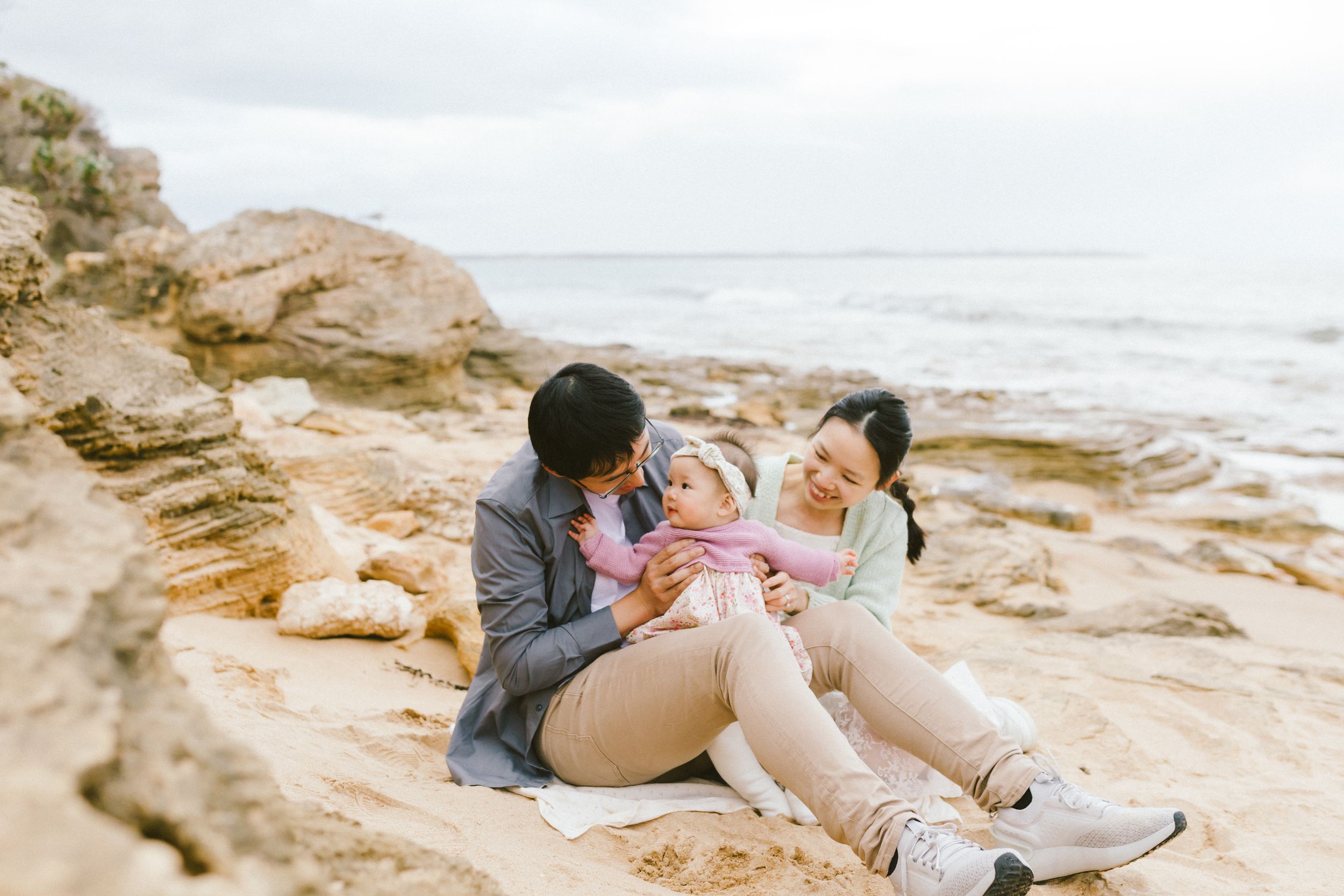 Couple sits together on rocky beach cliffs during sunset photoshoot at the ocean.