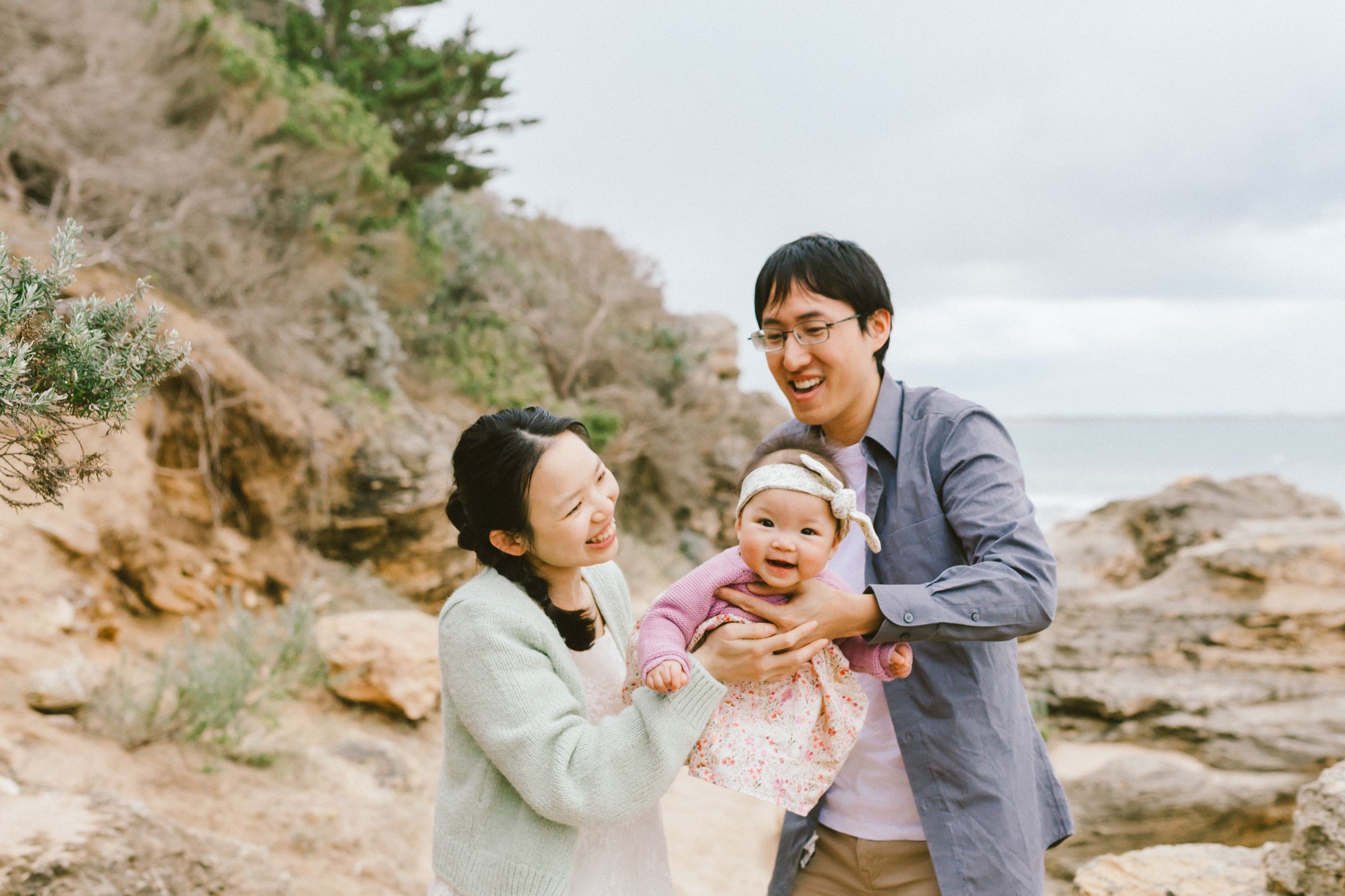 Family enjoys playful moments together on a rocky beach during sunset.