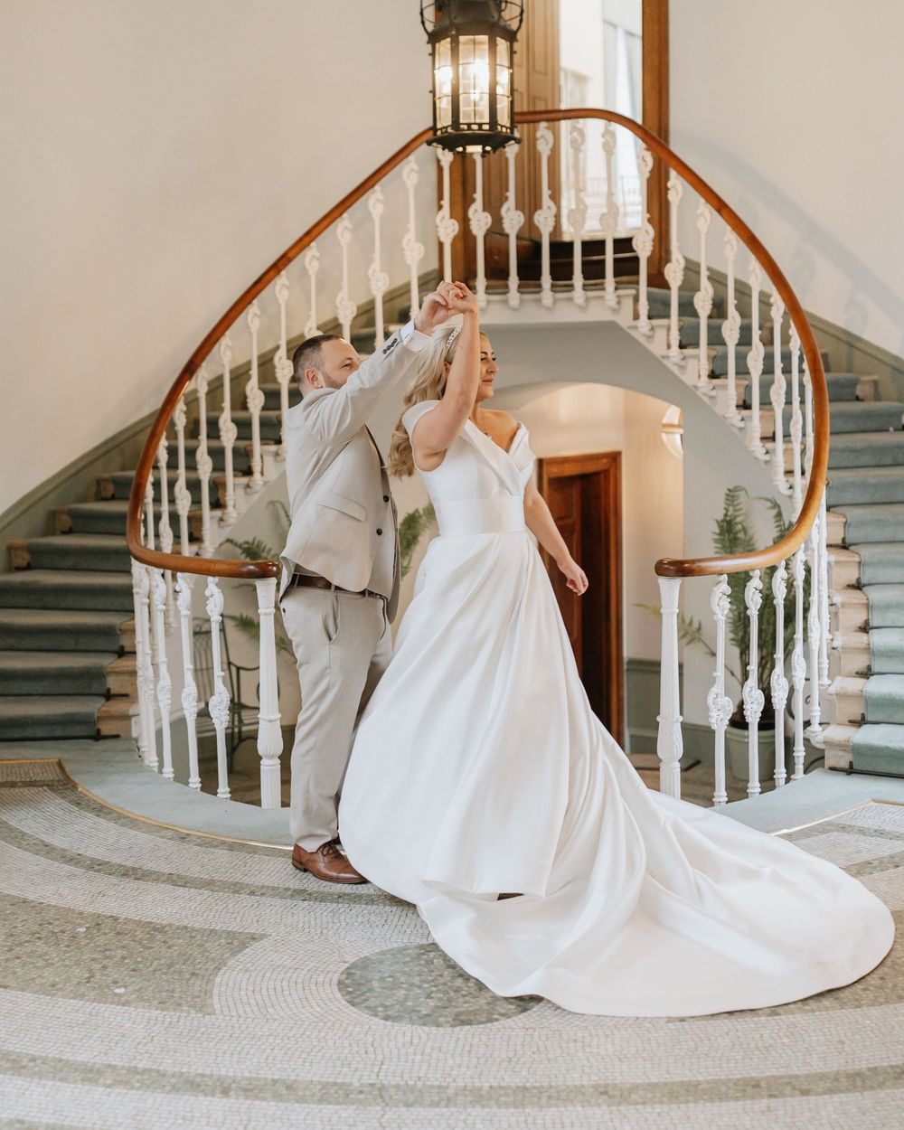 A couple in wedding attire share a romantic moment on an elegant curved staircase with white spindles.
