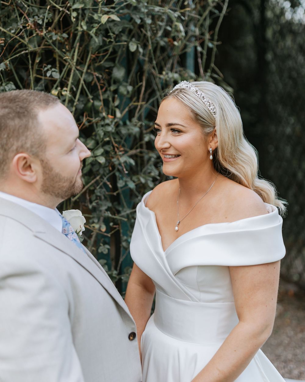 A couple in wedding attire laughs together during their outdoor photo session among green foliage.