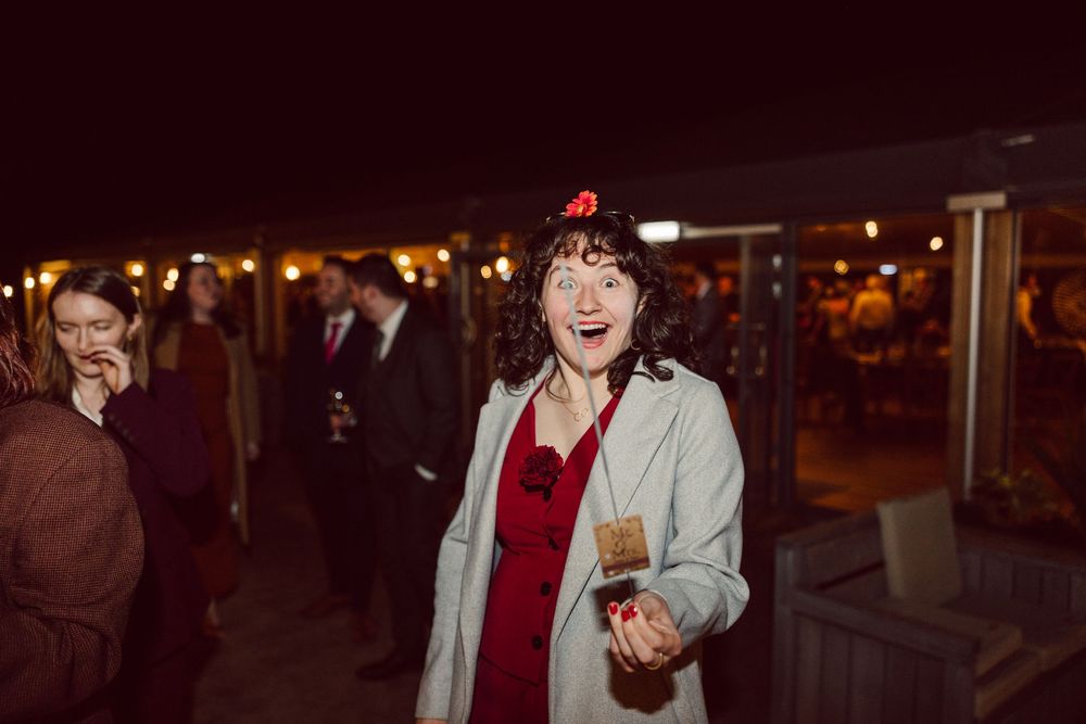 Person in a light jacket and red top laughs joyfully at a nighttime outdoor gathering.