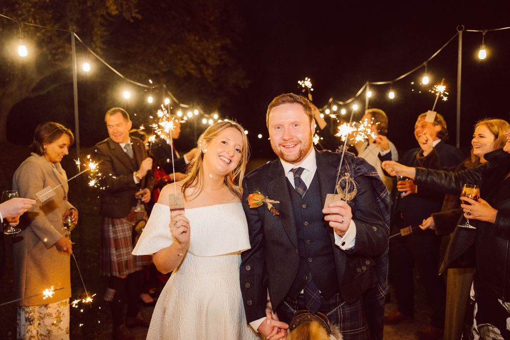 Wedding celebration at night with string lights and sparklers as couple celebrates with guests.