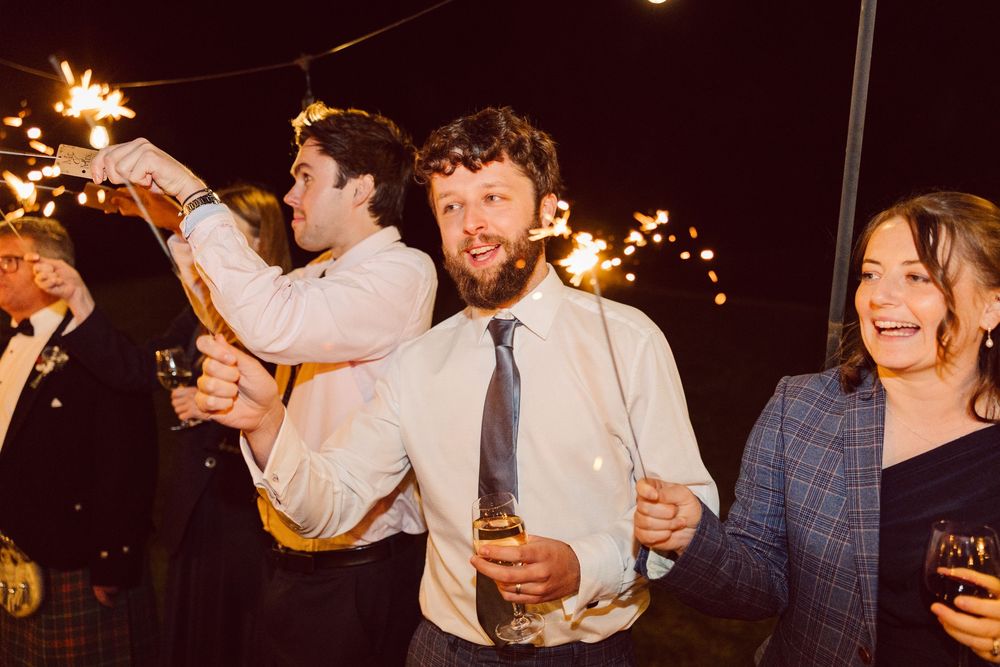 A group of people celebrating at a nighttime party with sparklers and drinks, creating a festive atmosphere.