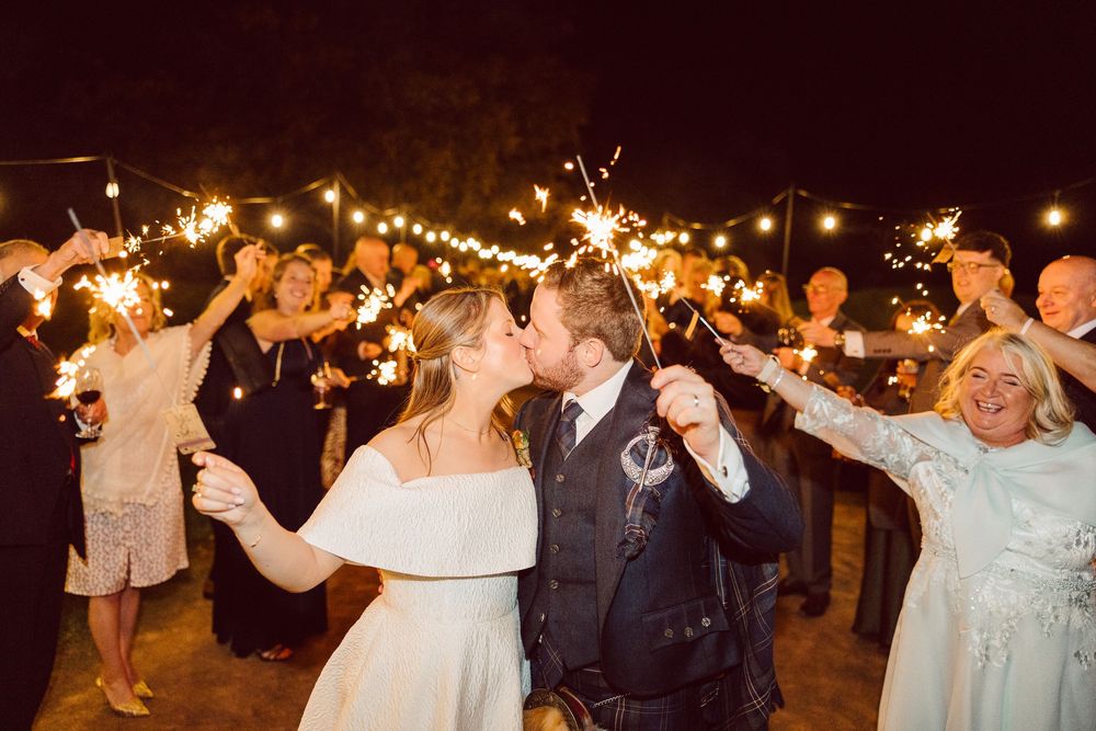 Wedding guests dance and celebrate on an outdoor dance floor illuminated by string lights during an evening reception.