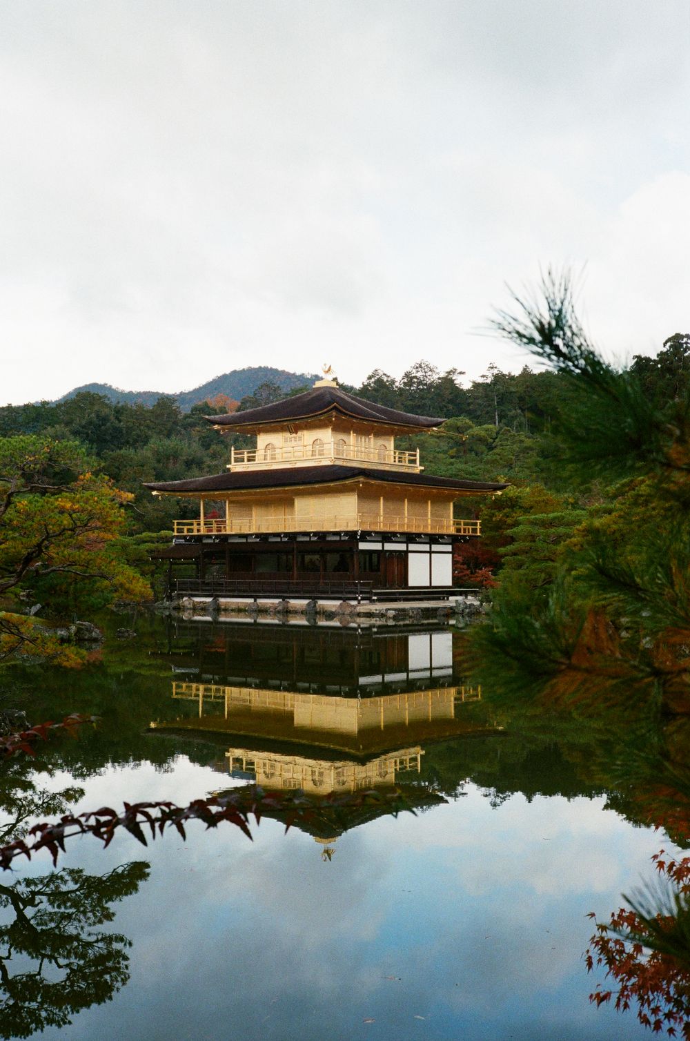 Golden Pavilion temple Kinkaku-ji reflects perfectly in still waters surrounded by autumn foliage in Kyoto, Japan.