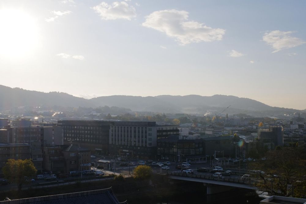 A panoramic cityscape view with mountains in the background and modern buildings under a partly cloudy sky.