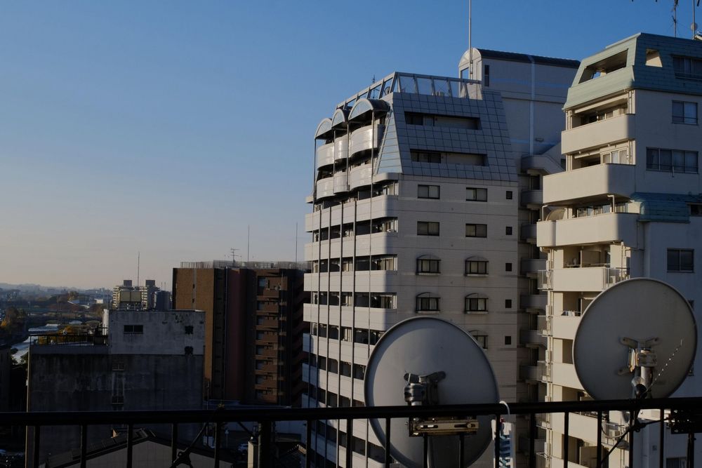 Modern apartment buildings with satellite dishes against a clear blue urban skyline.