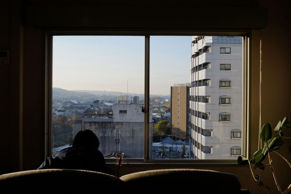 Panoramic cityscape view through a large window showing urban buildings and distant mountains.