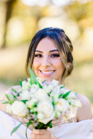 Beautiful smiling bride with updo holds white rose bouquet in golden outdoor setting.