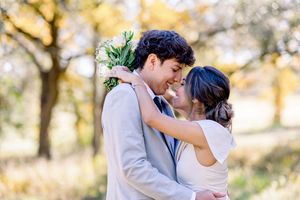 Romantic couple nearly kissing outdoors in autumn, groom holding white floral bouquet.