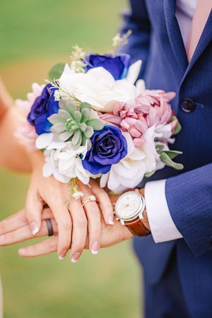 Close-up of bride and groom holding a colorful bouquet of blue, white, and pink flowers at their wedding.