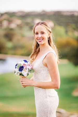 Elegant bride in a lace wedding gown holding a bouquet of blue and pink flowers outdoors at her wedding.