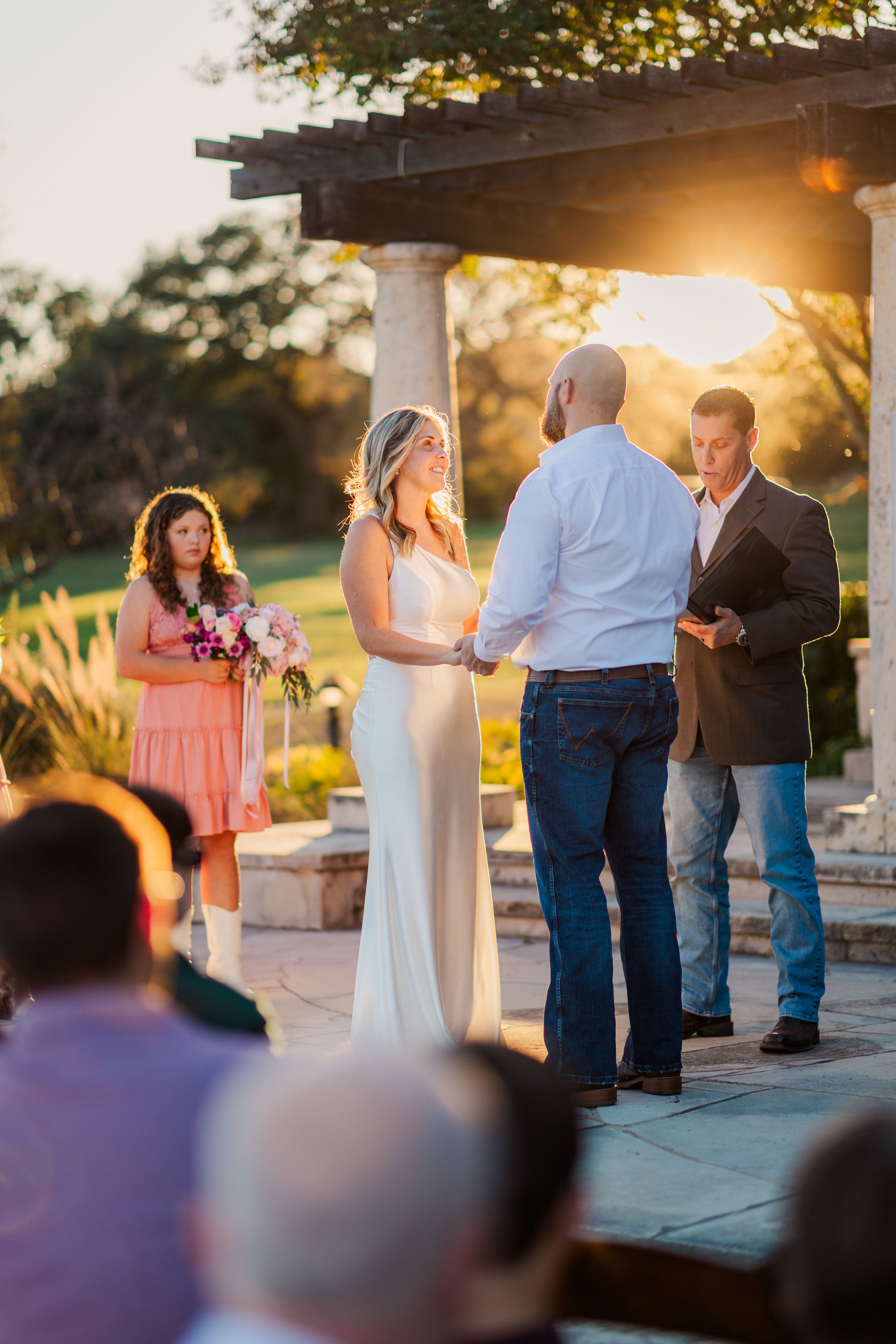 Bride and groom exchanging vows at sunset outdoor wedding ceremony under pergola.