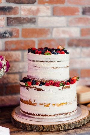 Two-tier naked wedding cake topped with fresh berries on rustic wood slice stand.
