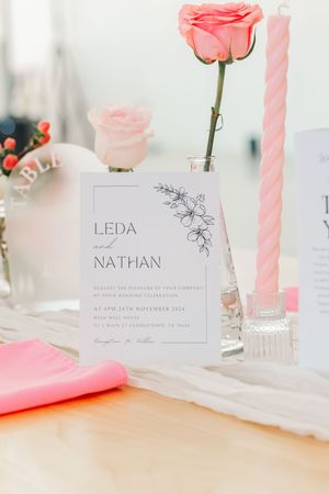 Elegant wedding invitation for Leda and Nathan displayed with pink roses and spiral candles.