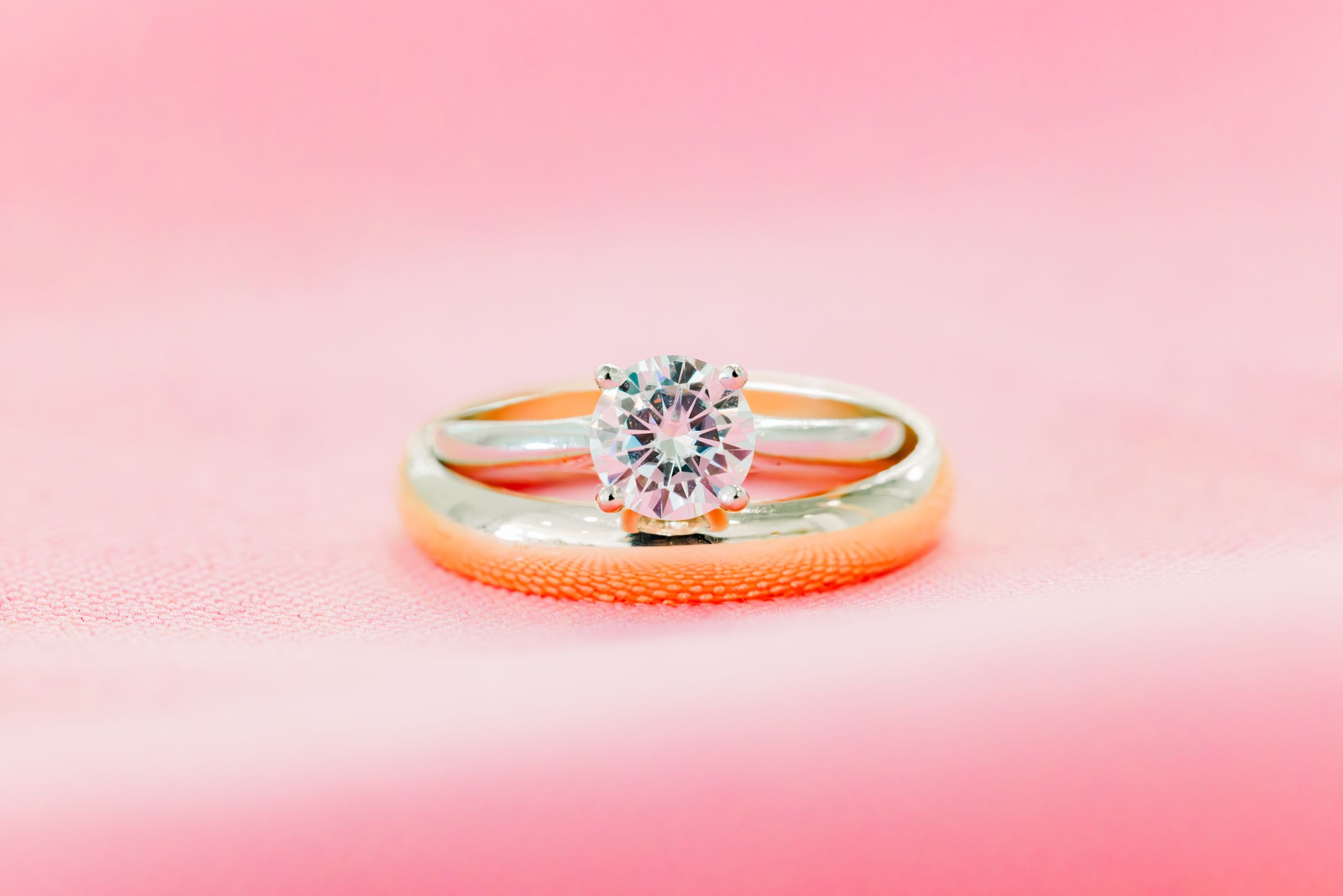 Gold solitaire diamond engagement ring with wedding band on pink background.