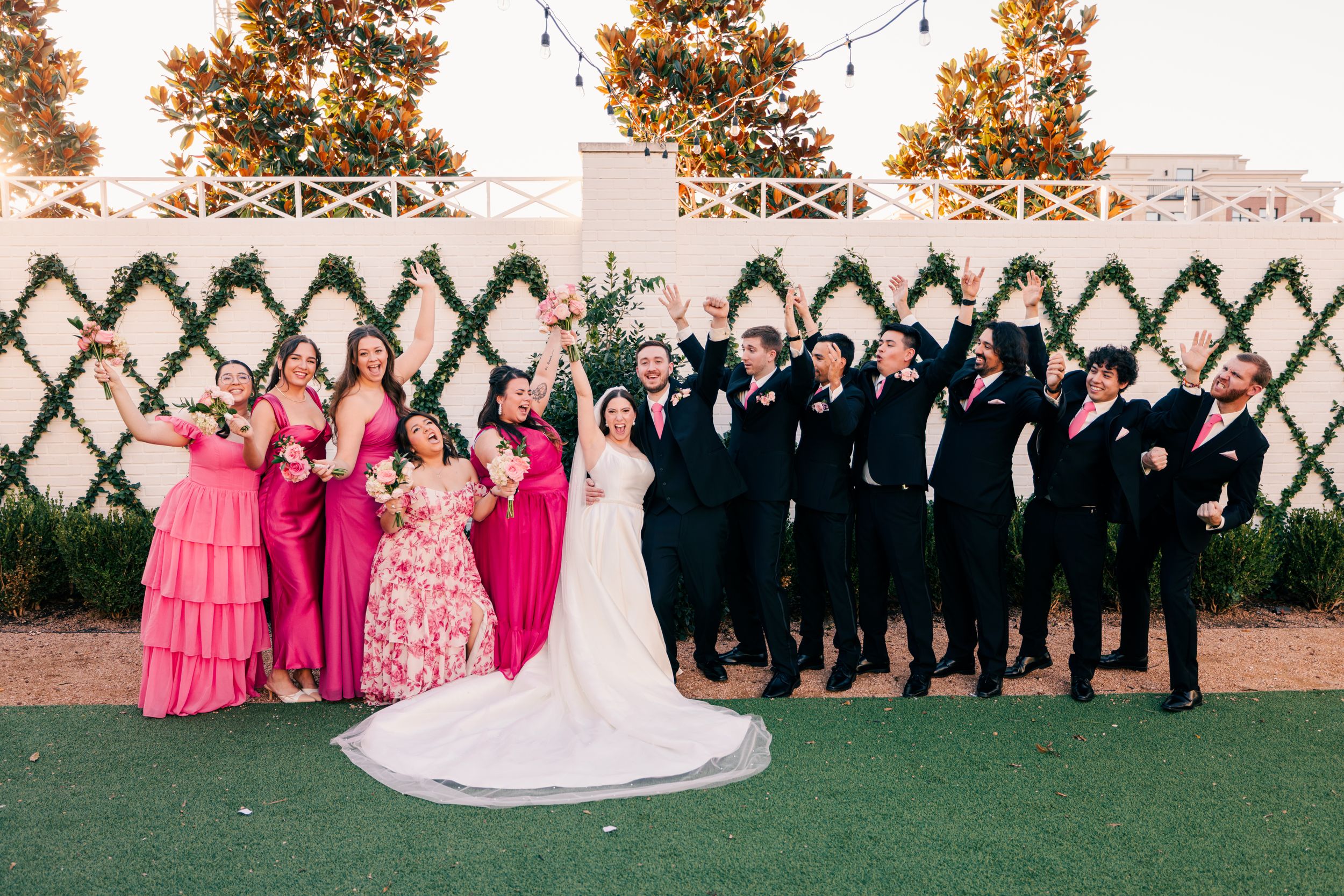 Wedding party in pink and navy celebrating outdoors with greenery backdrop.