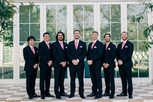 Seven groomsmen in black suits with pink ties posing together indoors.