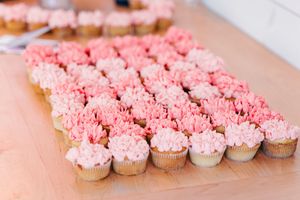 Rows of pink ombre frosted cupcakes arranged on a wooden table at a wedding reception.