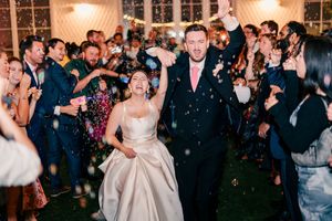 Bride and groom grand exit with confetti and sparklers surrounded by cheering guests.