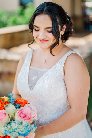Beautiful bride in sparkly white gown smiles softly while holding vibrant orange and pink bouquet.