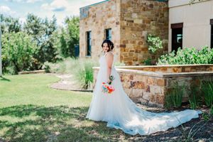 Elegant bride in white A-line gown with long train poses outdoors holding bright colorful bouquet.