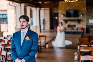 Groom in blue suit awaiting bride during first look moment at rustic indoor wedding venue.