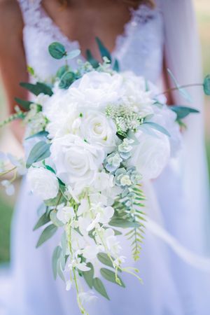 Bride holding elegant cascading white rose and eucalyptus wedding bouquet in lace gown.
