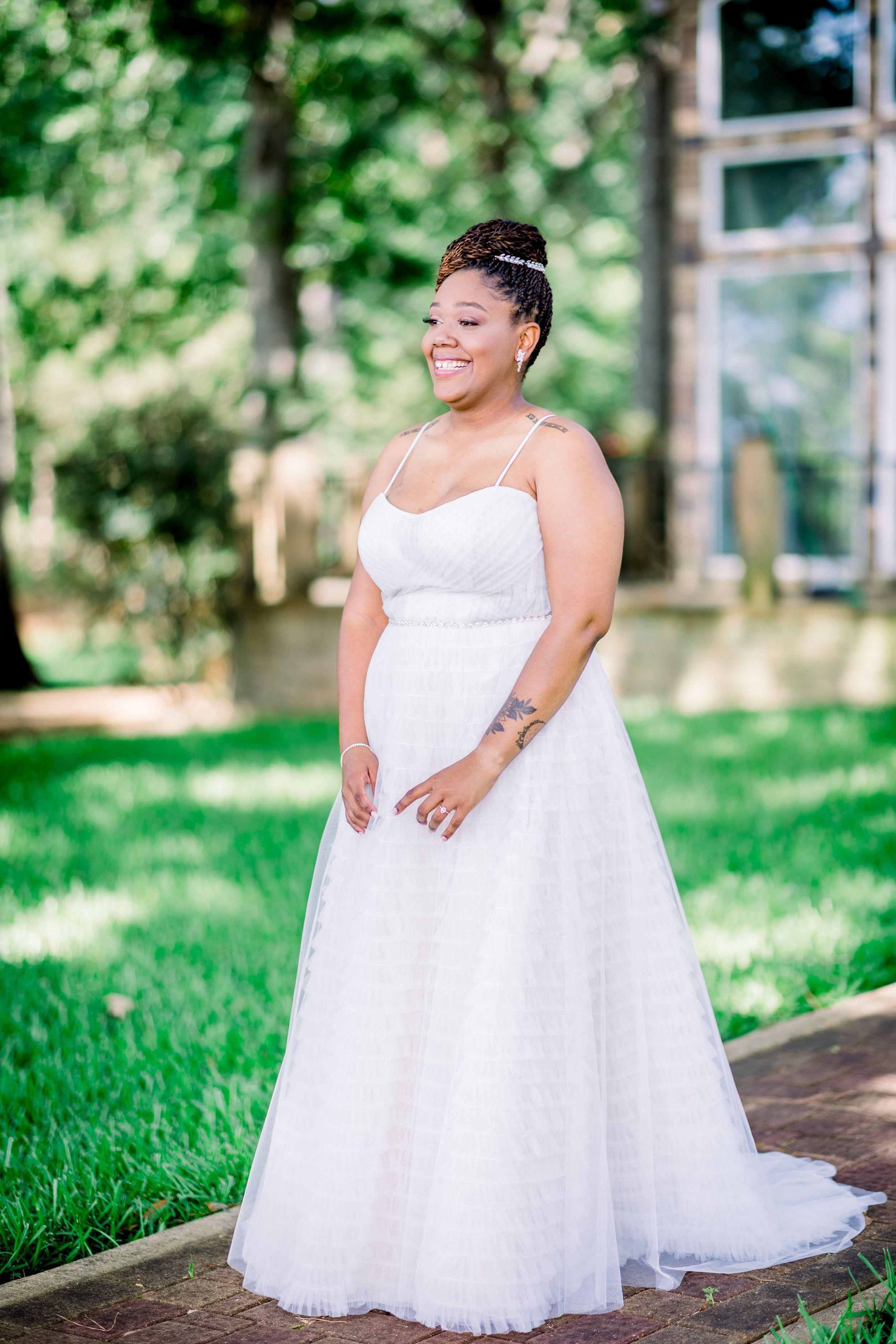 Smiling bride in strapless ball gown posing outdoors in lush green garden setting.