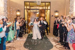 Bride and groom exit wedding venue through bubble send-off surrounded by cheering guests.