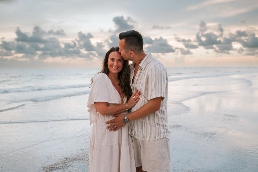 Romantic couple in white outfits embrace during sunset at a serene beach, creating intimate and dreamy moments together.