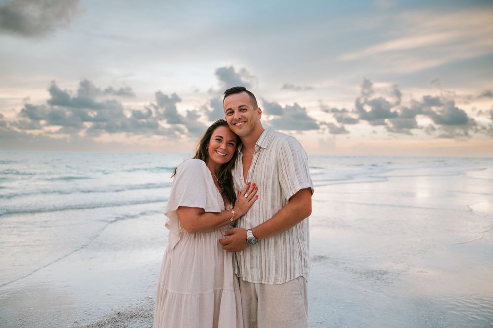 Romantic couple in white clothes walking and embracing on a serene beach at sunset with ocean waves in the background.