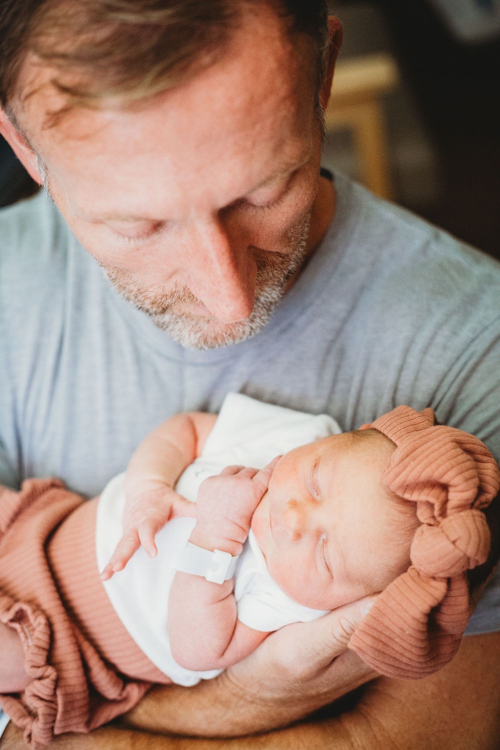 A tender moment shows a person in a gray shirt gently cradling and kissing a sleeping newborn baby.