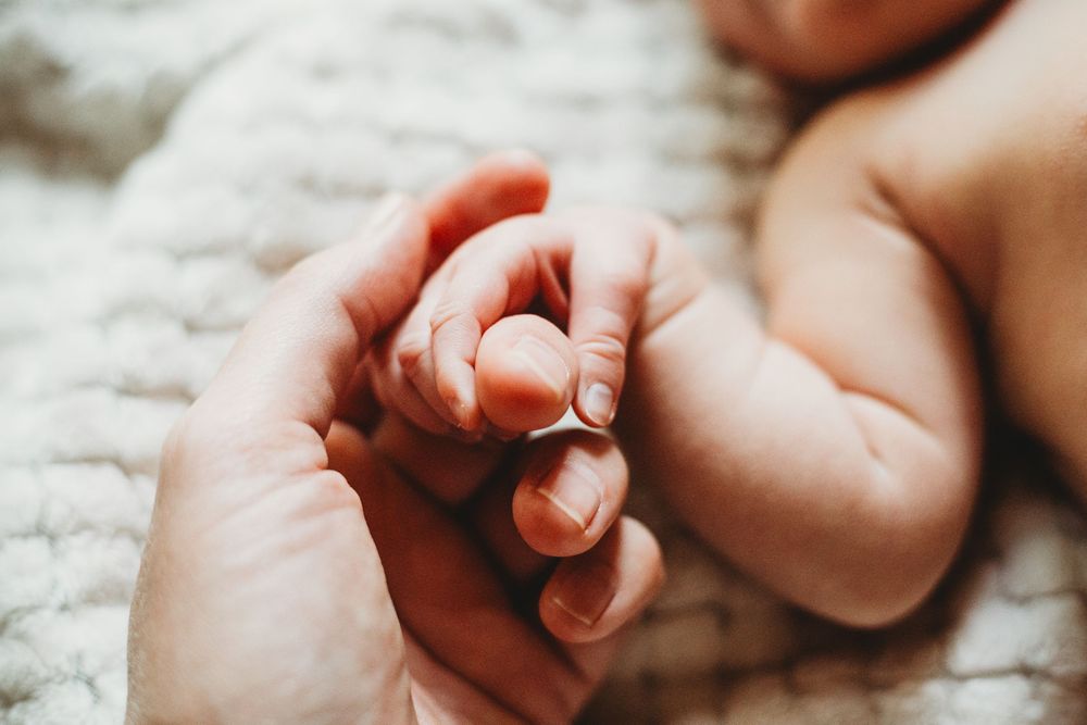 Close-up shot of a tiny newborn baby's feet and fingers with pure white blanket in the background.
