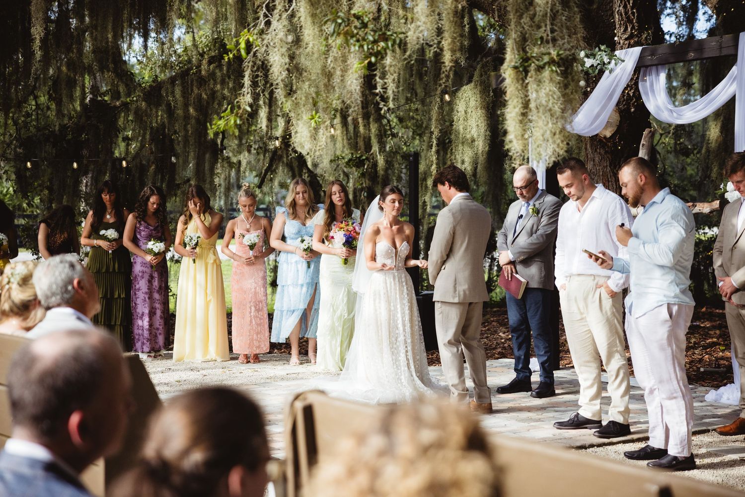 Wedding party gathered in an outdoor ceremony under moss-draped oak trees in Southern style setting.