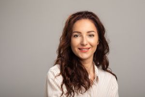 Portrait photo showing a woman with dark wavy hair and natural smile in casual attire.