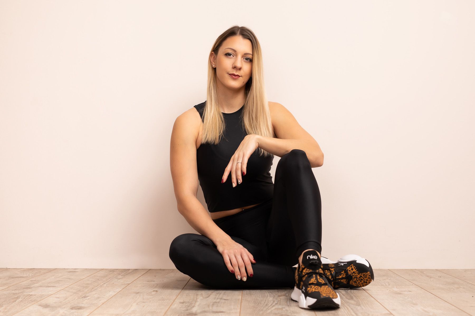 Person in black athletic wear sitting against white wall in minimalist artistic photo series.