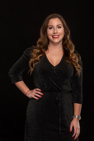 A confident person poses in a sparkly black formal dress against a dark background in a professional studio setting.