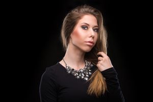 Model wearing a statement crystal necklace with black top poses against dark background in dramatic lighting.