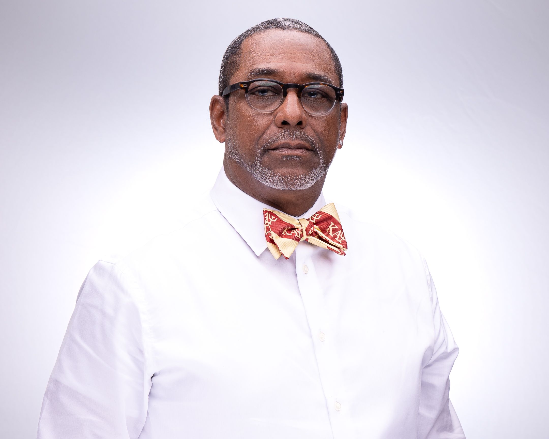 Medical professional in white coat and glasses photographed in studio setting.