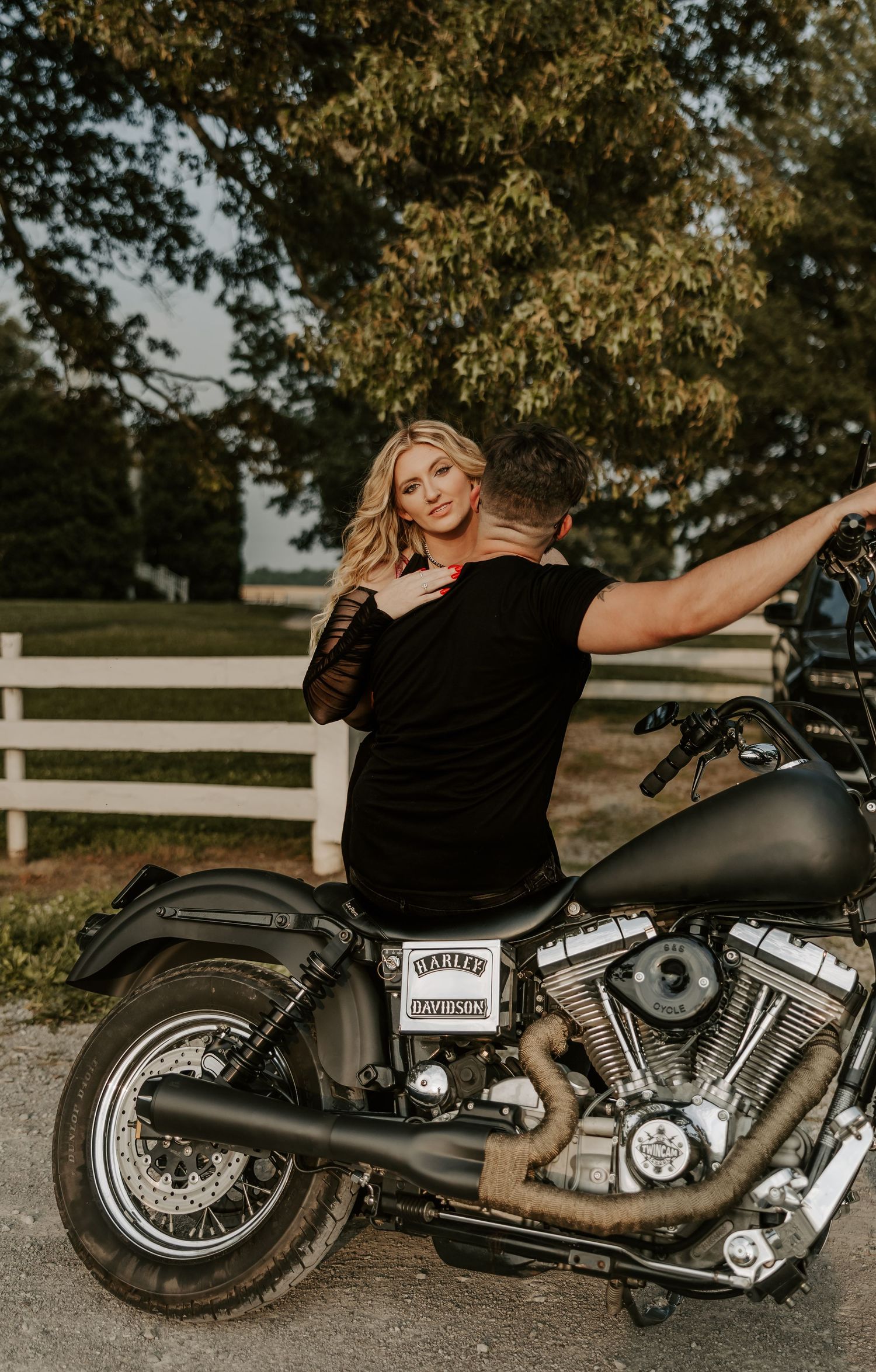 A custom black motorcycle displayed against a scenic backdrop with white fencing and trees.