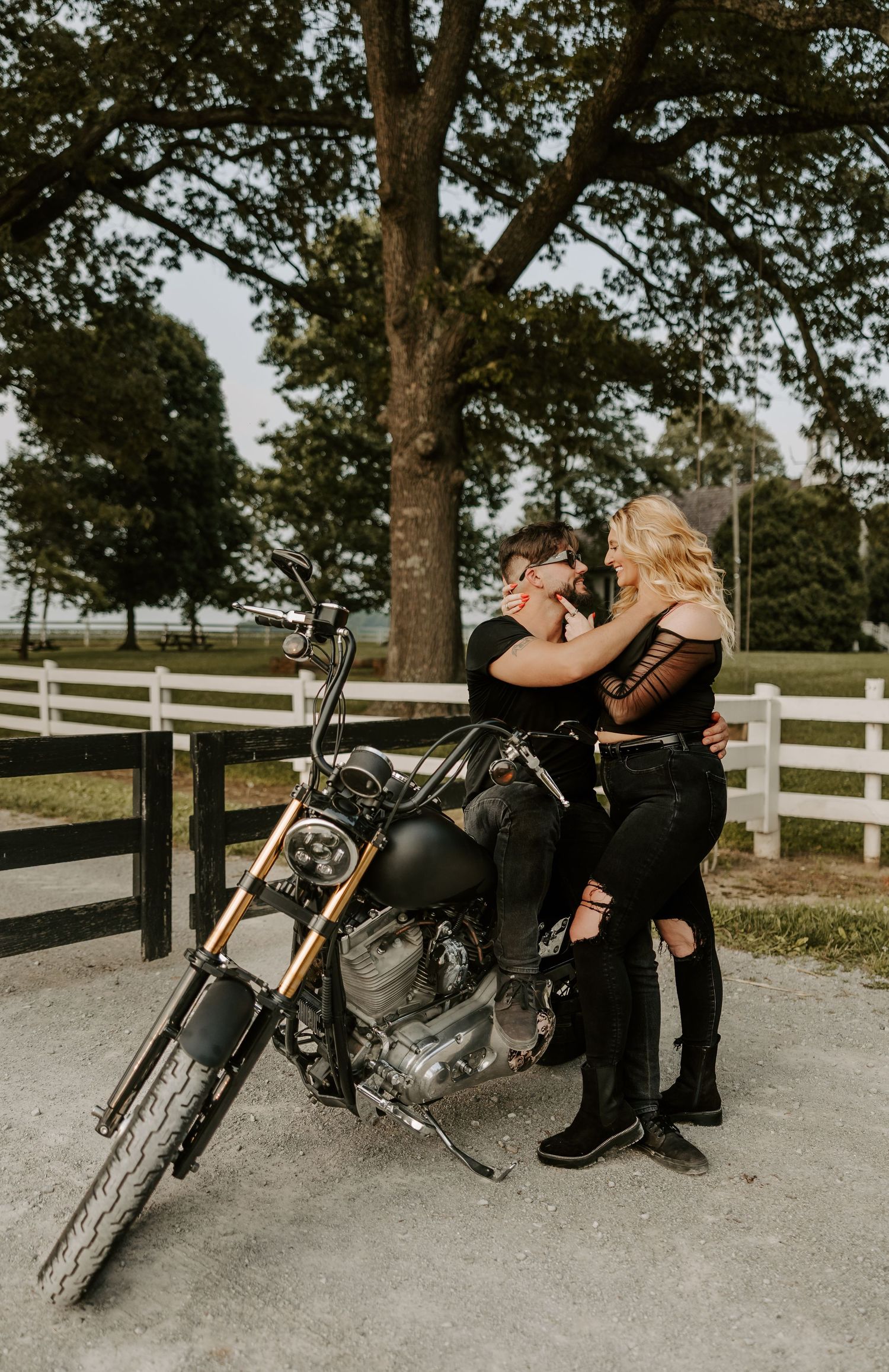 A stylish motorcycle photoshoot featuring a black bike on a gravel path with white fencing.