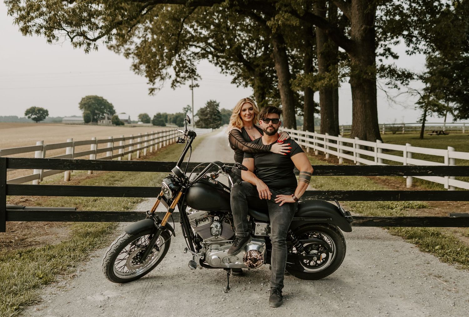 A motorcycle parked near white fencing with trees in the background during a countryside photoshoot.